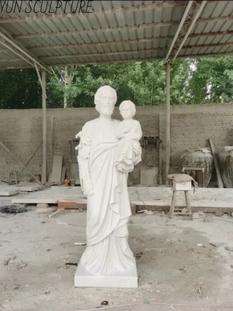 A hand-carved Saint Joseph and Child Jesus statue made of Hanbaiyu white marble in a workshop, showcasing the stone's natural warm cream tone.