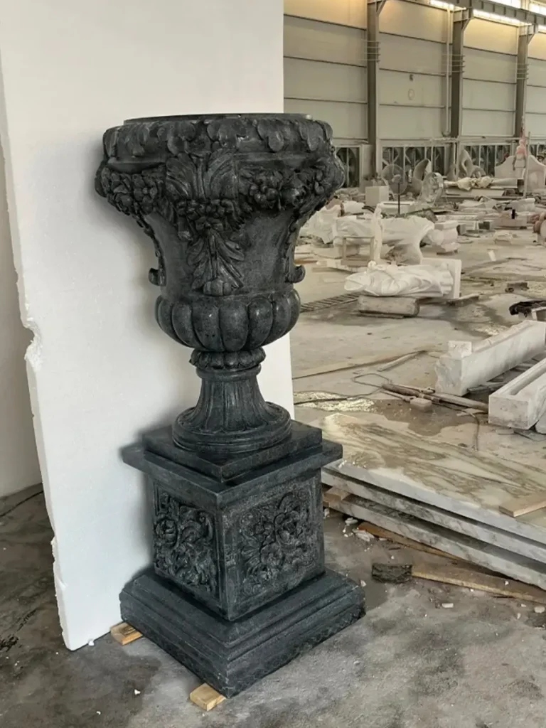 A handcrafted black granite garden urn and planter on a pedestal, showcased in a professional stone carving workshop before final installation.