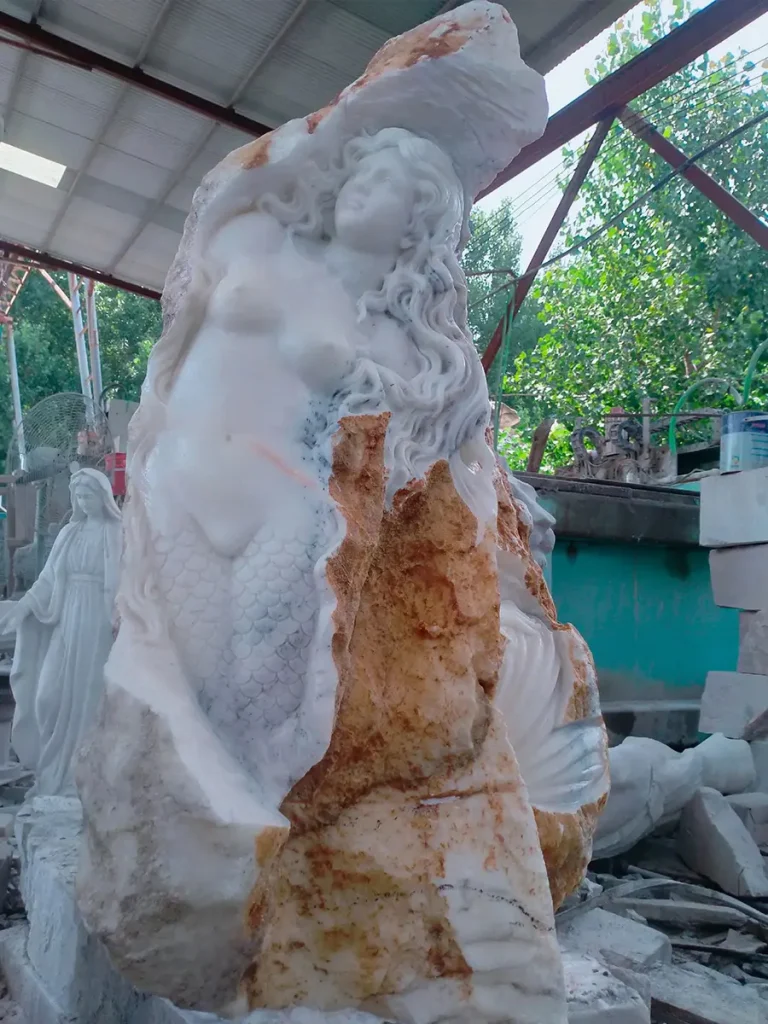 A large-scale marble mermaid statue under construction in the Yun Sculpture workshop, showing the transition from raw stone to fine art.