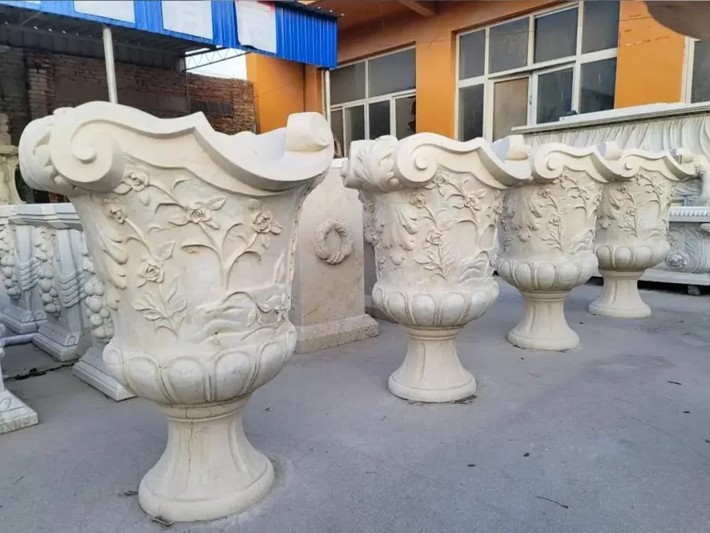 A row of hand-carved white marble flower pots with decorative scroll handles, demonstrating the frost-proof resilience of dense natural stone.