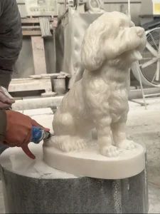 Craftsman carving a white marble dog.