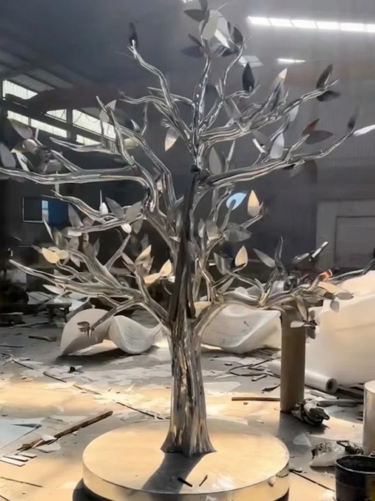 A partially finished stainless steel tree sculpture with individually forged metal leaves being attached to the branches. Using the traditional Repoussé method, each leaf is uniquely curved to catch the light differently, ensuring the canopy is never uniform.