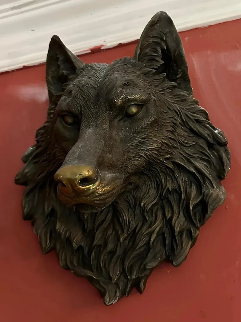 An angled view of a finely crafted bronze wolf bust serving as architectural wall decor. The polished, golden hue on the wolf's snout highlights how real bronze develops a unique, beautiful patina over time, elevating the piece far beyond a simple decorative object.