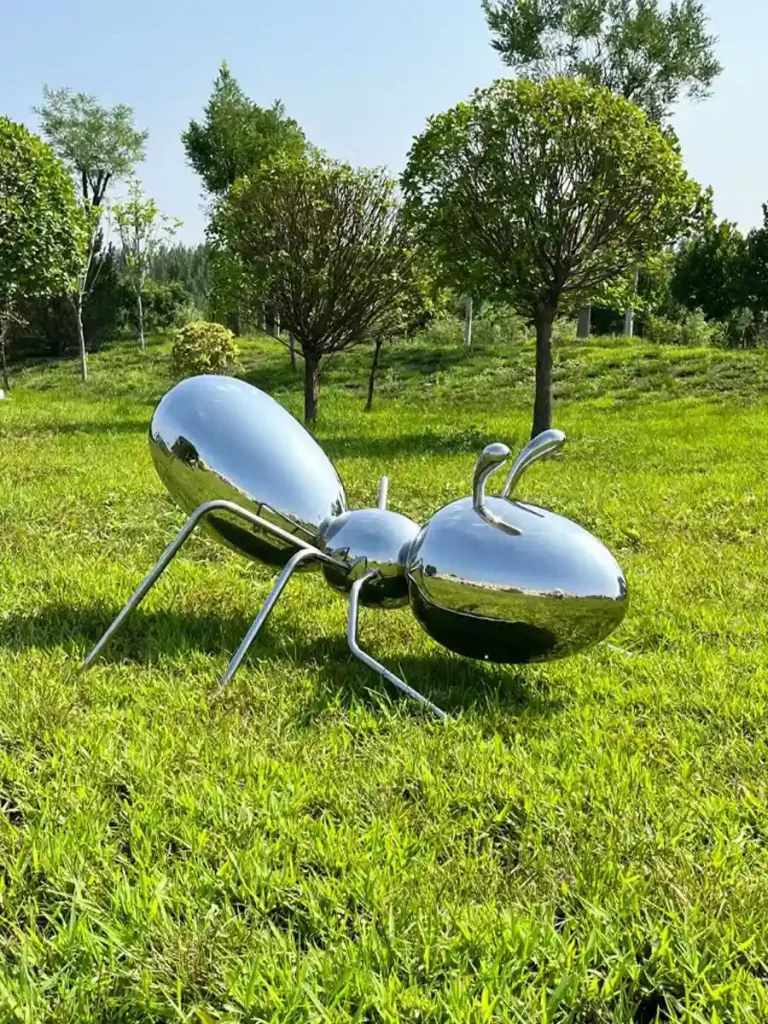 A highly reflective stainless steel metal sculpture of an ant in a bright garden setting. This piece beautifully showcases the structural resilience and near-perfect light interaction achieved when premium materials are expertly crafted for exterior landscape architecture.