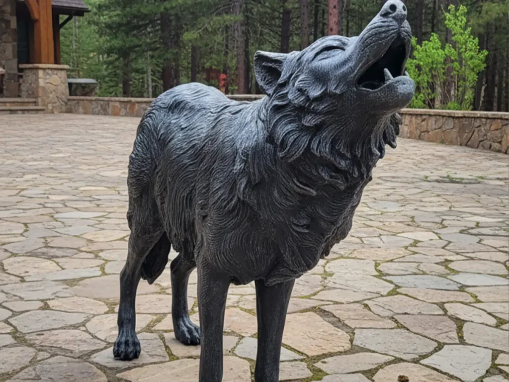 A majestic bronze wolf sculpture howling on a stone patio outside a luxury mountain lodge. With alert ears and a grounded posture, this monumental animal statue symbolizes vigilance and protection, guarding the untamed land and the people who gather there.