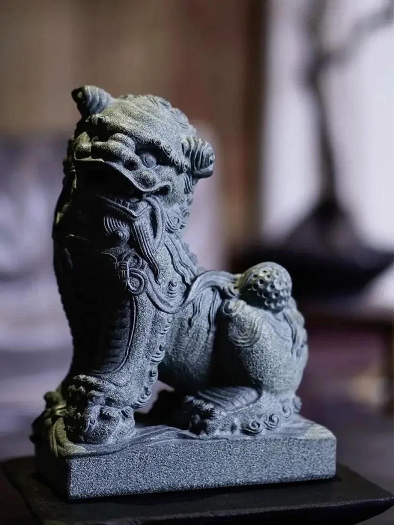 A finely carved, dark granite Foo Dog in the Southern Hui'an style. The intricate miniature sculpture features a lively posture with a tousled mane and open mouth, highlighting the region's detailed stone hollowing techniques.