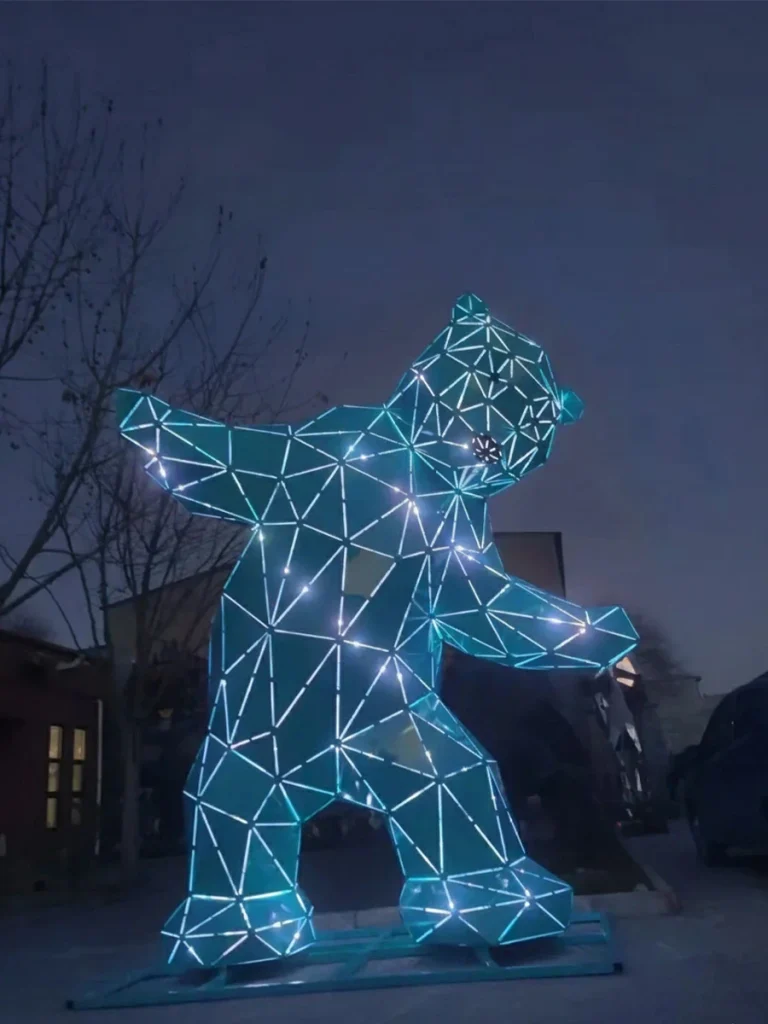 A modern, low-poly metal bear sculpture brightly illuminated with glowing LED lights at night. This striking integration of technology and art transforms the bear's universal symbolism of strength into a contemporary public landmark, cementing the identity of modern urban spaces after dark.