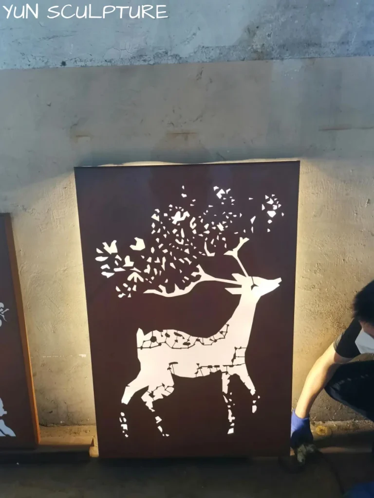 A backlit rusted metal wall panel depicting a deer and forest motif, illustrating how grazing light transforms minimalist metal art into an immersive visual environment.