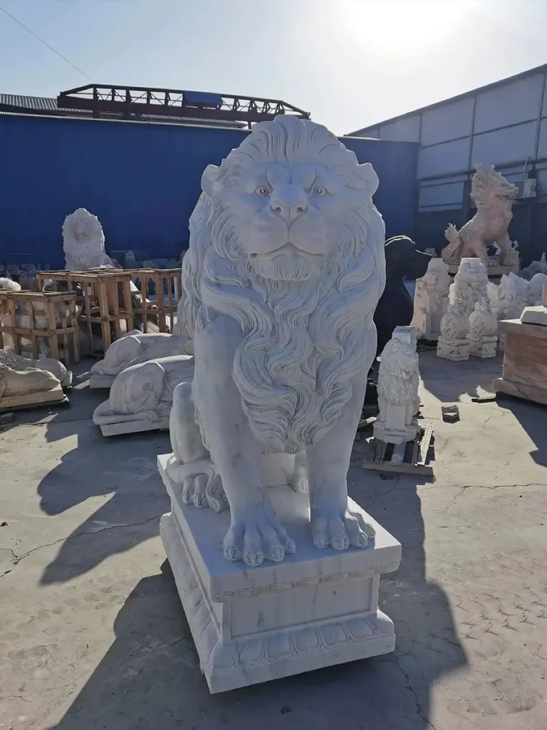 Direct front view of an imposing white marble outdoor lion statue bathed in sunlight. The sculpture features exceptionally broad shoulders and a voluminous carved mane, perfectly illustrating how bulk and physical presence are essential for balancing large estate gates.