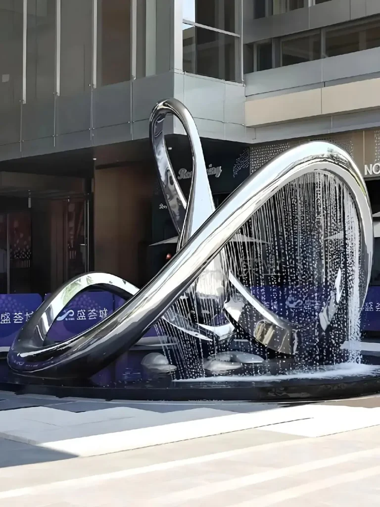 A mesmerizing mirror-polished stainless steel infinity ring fountain illuminating a modern courtyard at dusk. Water flows evenly from the upper edge of the continuous loop to form a perfect, transparent water curtain, creating a simple yet hypnotic geometric centerpiece.