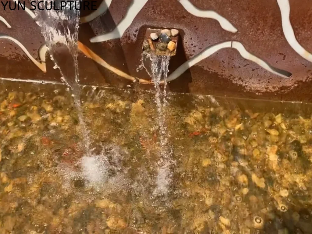 An extreme close-up of clear water splashing from a Corten steel fountain spout onto submerged river stones. Whether allowing the patina to fully stabilize naturally or applying an internal Polyurea safety coating, these expert engineering steps guarantee that rust runoff does not compromise the delicate aquatic systems.