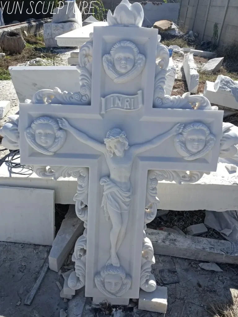 An incredibly ornate white marble Jesus statue featuring four intricately carved cherub faces at the ends of the cross. This demanding sculptural masterpiece perfectly illustrates the unforgiving labor economics of marble carving, where every chisel strike is a permanent subtraction and requires master-level precision.