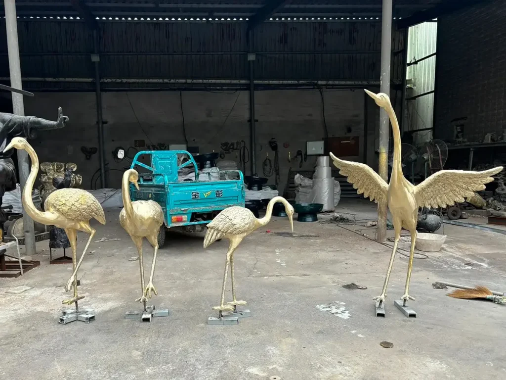 A collection of tall, slender Japanese crane sculptures in a foundry setting. Their elongated legs and graceful silhouettes create a dramatic visual rhythm, offering timeless elegance and a sense of enduring calm for contemporary or oriental gardens.