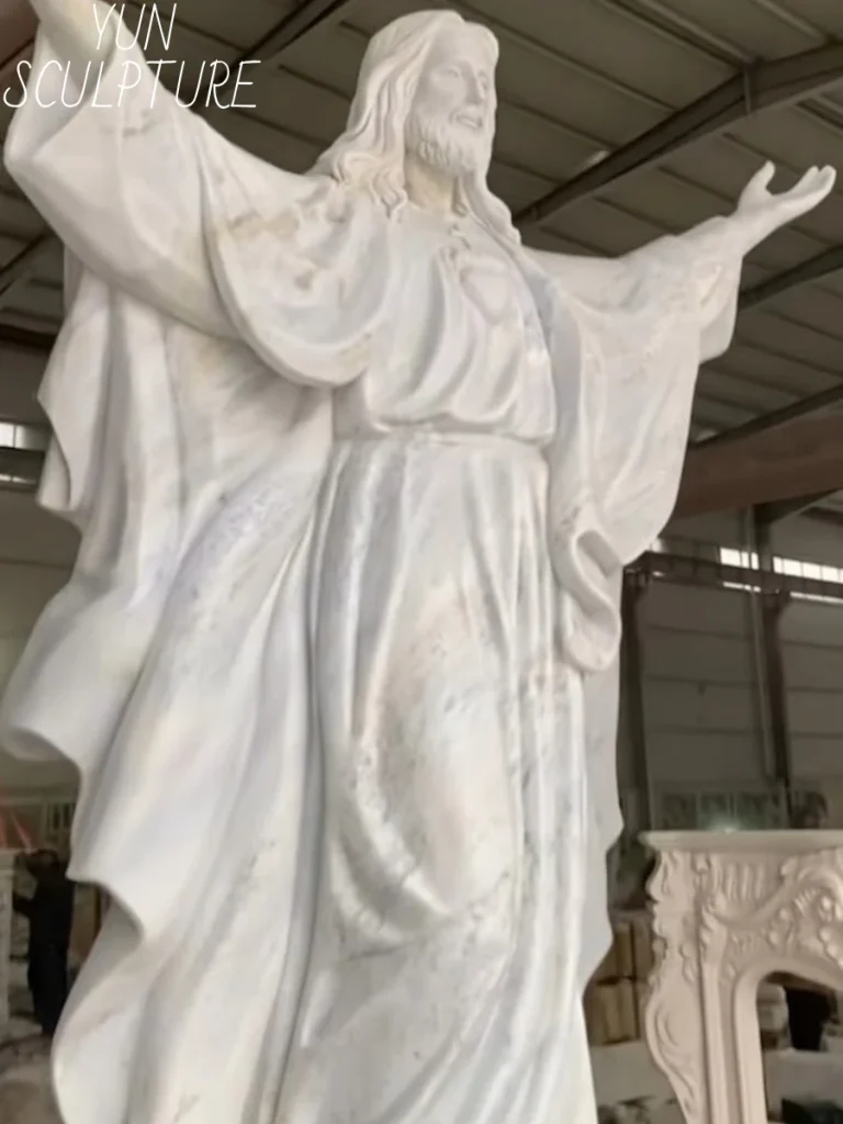 An angled close-up of a large jesus marble statue, highlighting the incredibly deep, delicate folds of the robe. This intricate surface detail demonstrates why placing a porous stone statue outdoors in freeze-thaw cycles or coastal climates will inevitably lead to devastating erosion and structural dissolution over decades.