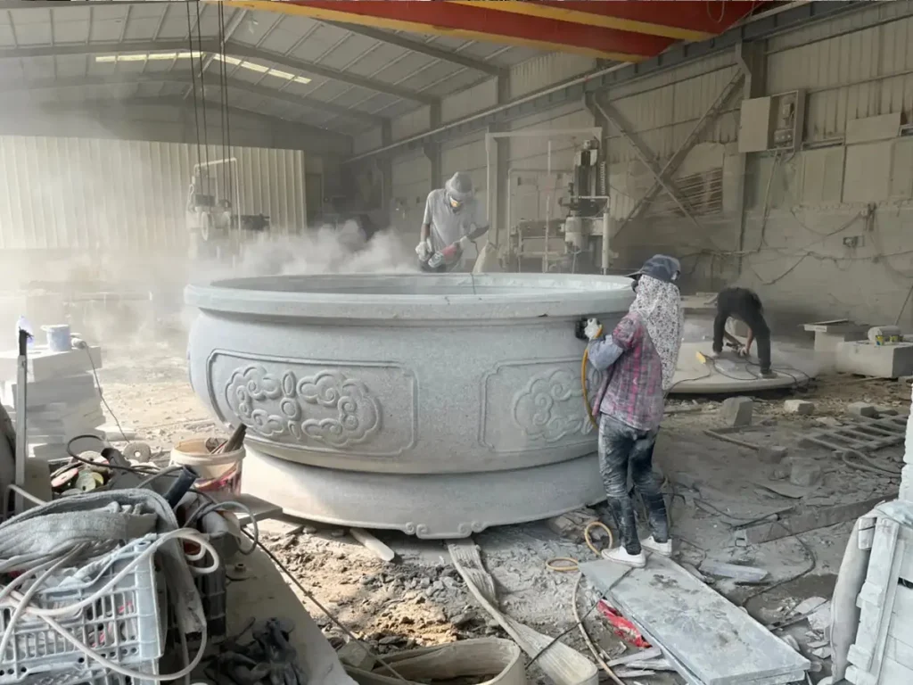 Skilled artisans at Yun Sculpture using professional tools to hand-finish a massive custom stone planter in the workshop, highlighting large-scale fabrication capabilities.