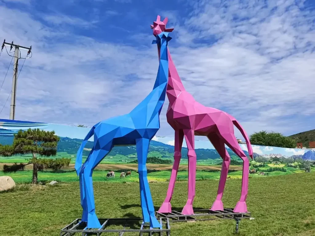 A pair of large blue and pink low-poly stainless steel giraffe sculptures standing outdoors on metal structural bases. In expansive estates, this kind of towering vertical presence acts as a vibrant architectural landmark visible from distant garden paths.