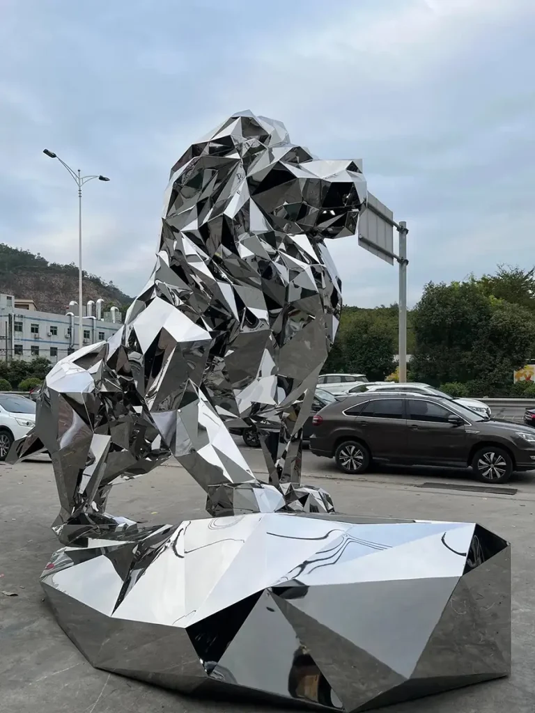 Full view of a massive geometric stainless steel lion sculpture standing dynamically on a matching faceted metal base. The mirror-polished surface provides exceptional corrosion resistance and structural strength, making it a dramatic, low-maintenance centerpiece for luxury estate entrances.