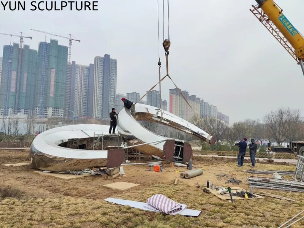 On-site installation of a large metal ring sculpture using a crane to align heavy segments, where full penetration welding will be used to ensure structural continuity.