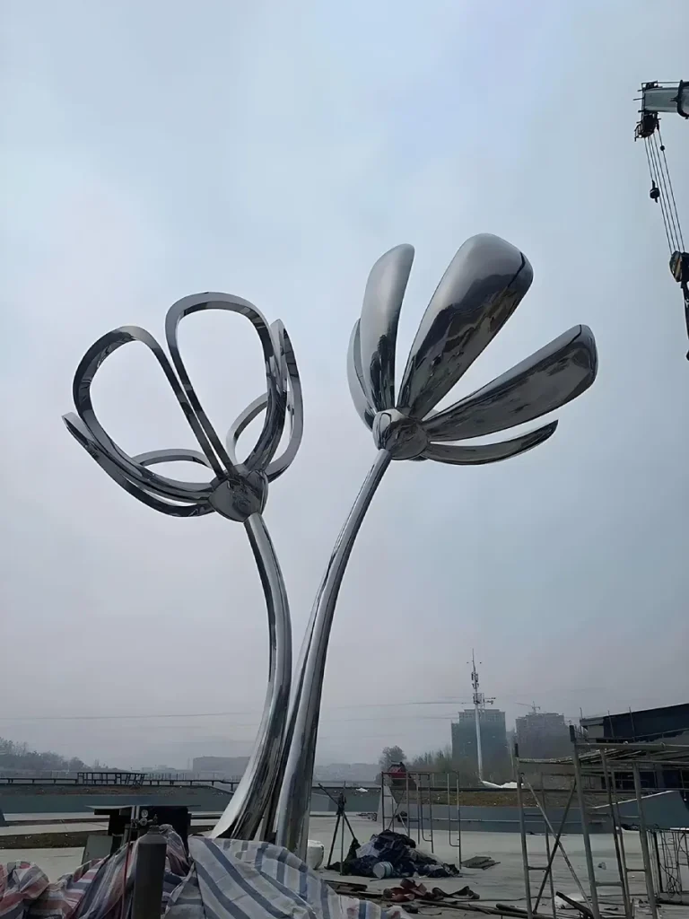 A monumental mirror-polished stainless steel floral sculpture standing outdoors. Its massive, sail-like petals and slender curved stems perfectly demonstrate why any large metal tree sculpture outdoor requires rigorous wind resistance engineering and a hidden internal structural skeleton to prevent stress failures at connection points.