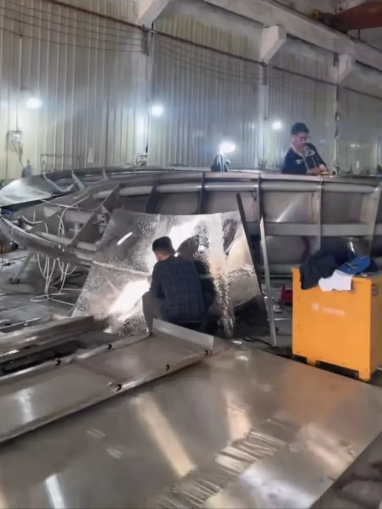  Factory workers meticulously welding the mirror-polished outer metal skin to the robust internal structural skeleton of a massive ring sculpture. This crucial step in fabricating large outdoor metal sculptures for sale hides the complex engineering beneath a flawless aesthetic surface.