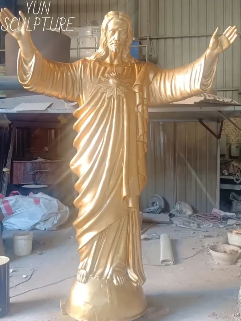 A monumental, golden-hued bronze risen christ outdoor statue standing with fully outstretched arms in a vast foundry workshop. The individual bronze sections have been expertly TIG welded together, perfectly demonstrating the massive scale and structural integrity required to support its heavy bronze skin during large-scale assembly.