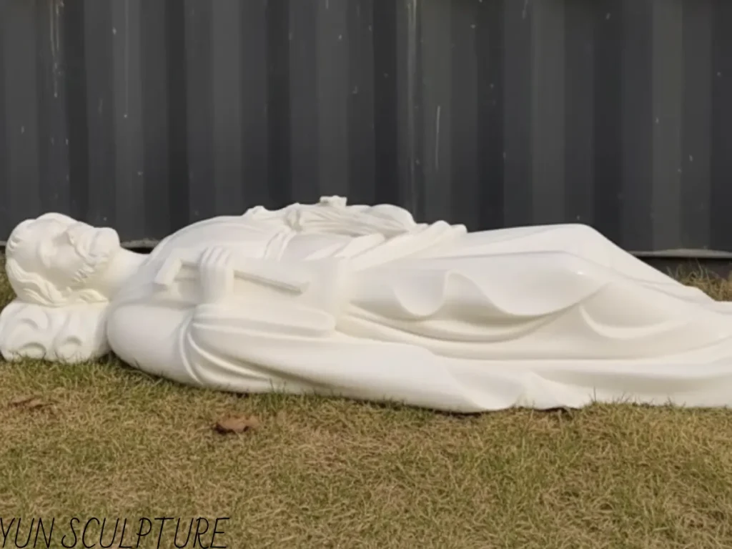 A large, white sleeping St. Joseph statue resting on the grass prior to installation. This larger institutional scale, known as the "community Joseph," is designed to become a shared focal point of prayer in chapels or monasteries once mounted on its elongated base.
