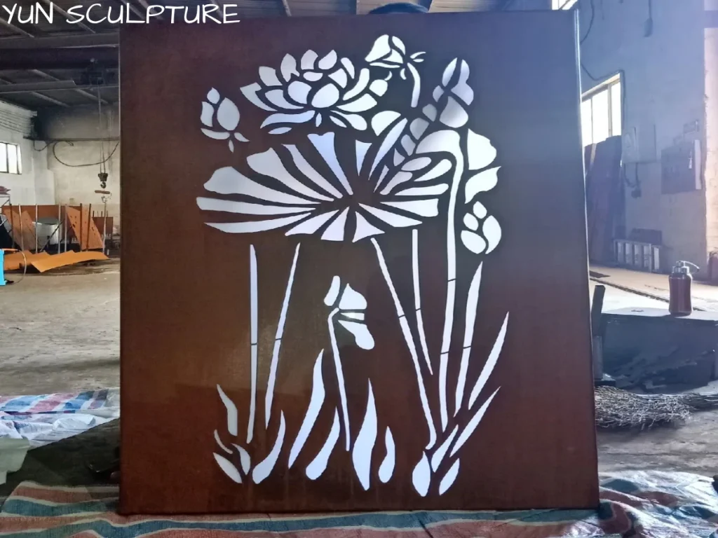 A freshly cut corten steel panel depicting a lotus flower resting on a workshop floor before shipping. The intricate wide cutouts demonstrate how the opaque steel will contrast with the areas that release light when used as backlit art.