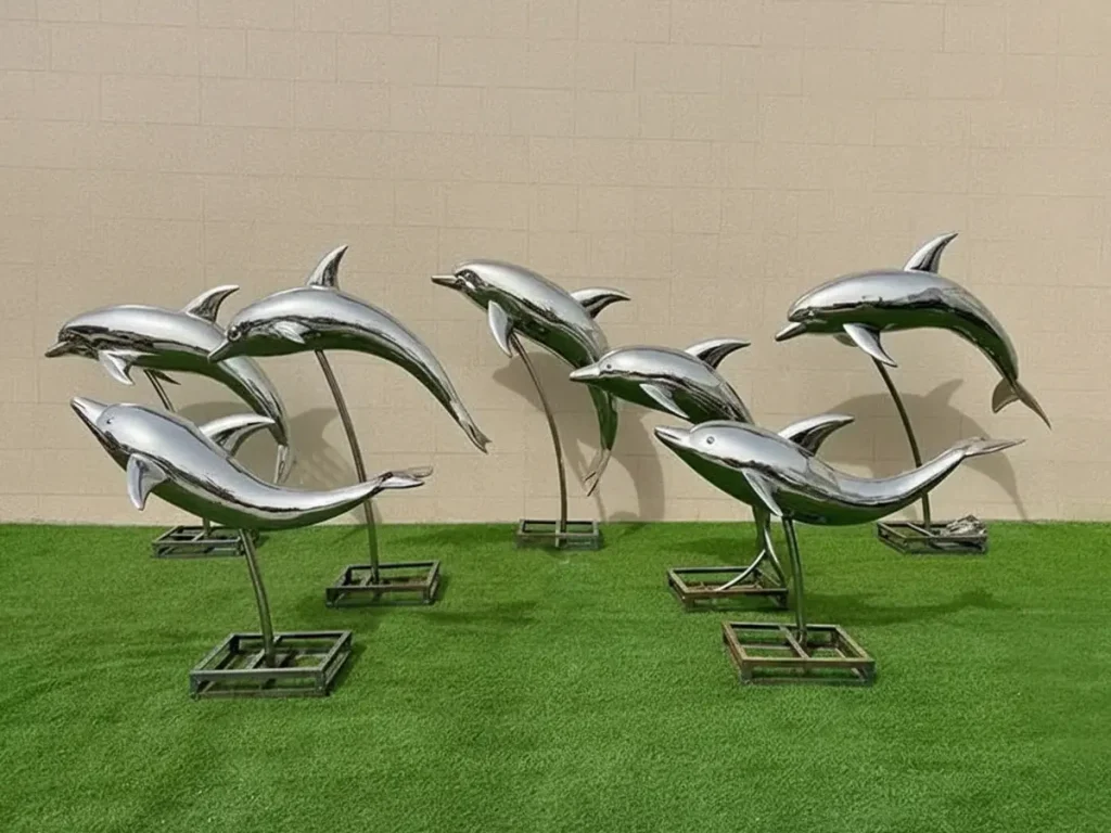 A pod of large, reflective stainless steel dolphin sculptures mounted on individual stands in a yard. Their dynamic, arcing forms are specifically designed to be positioned at the edge of infinity pools, visually merging the artwork with the ocean horizon.