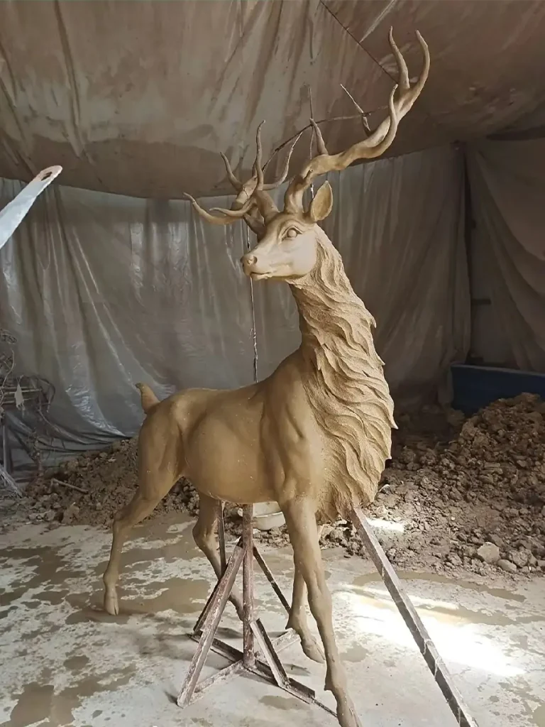 Full-body clay model of a life-size stag statue in a workshop. It showcases the distinctive silhouette with a raised neck and dramatic antlers, capturing the noble essence before being cast in bronze.