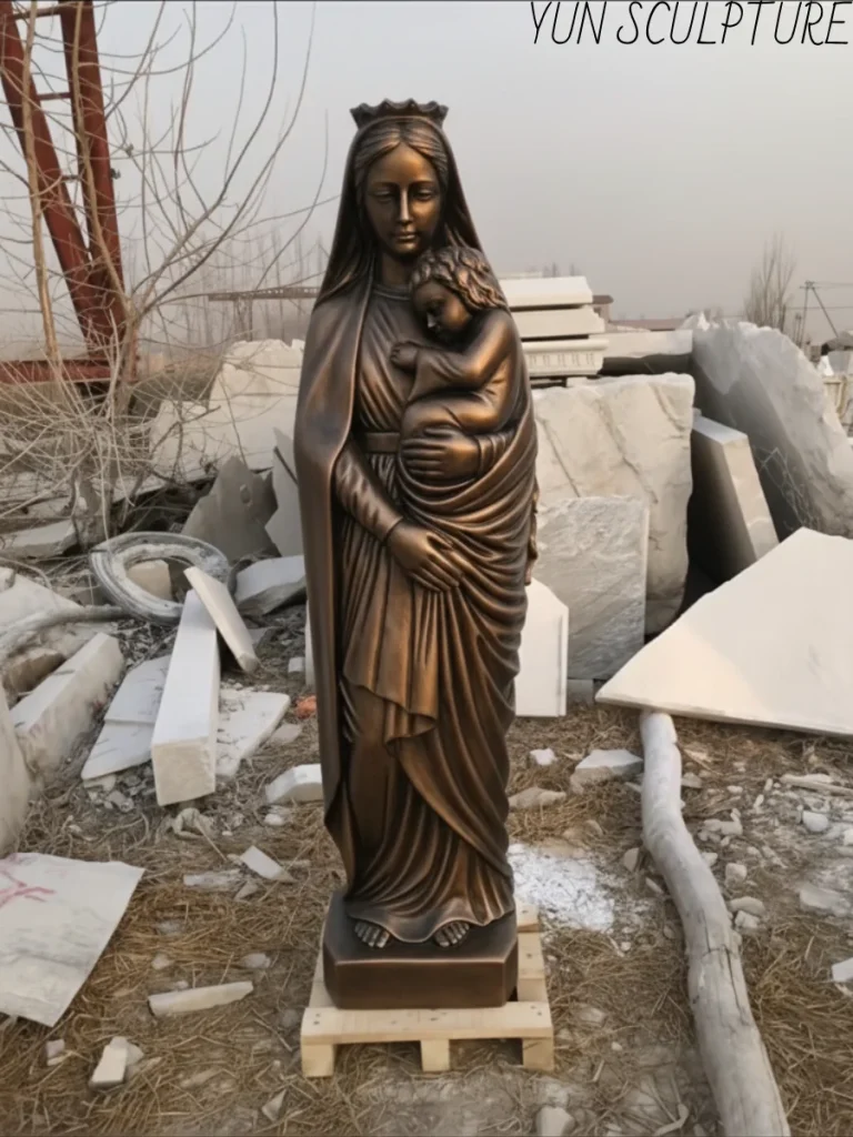 A life-size bronze statue of the Virgin Mary holding baby Jesus, featuring a multi-toned patina that distinguishes the Virgin's robes from the infant's form.