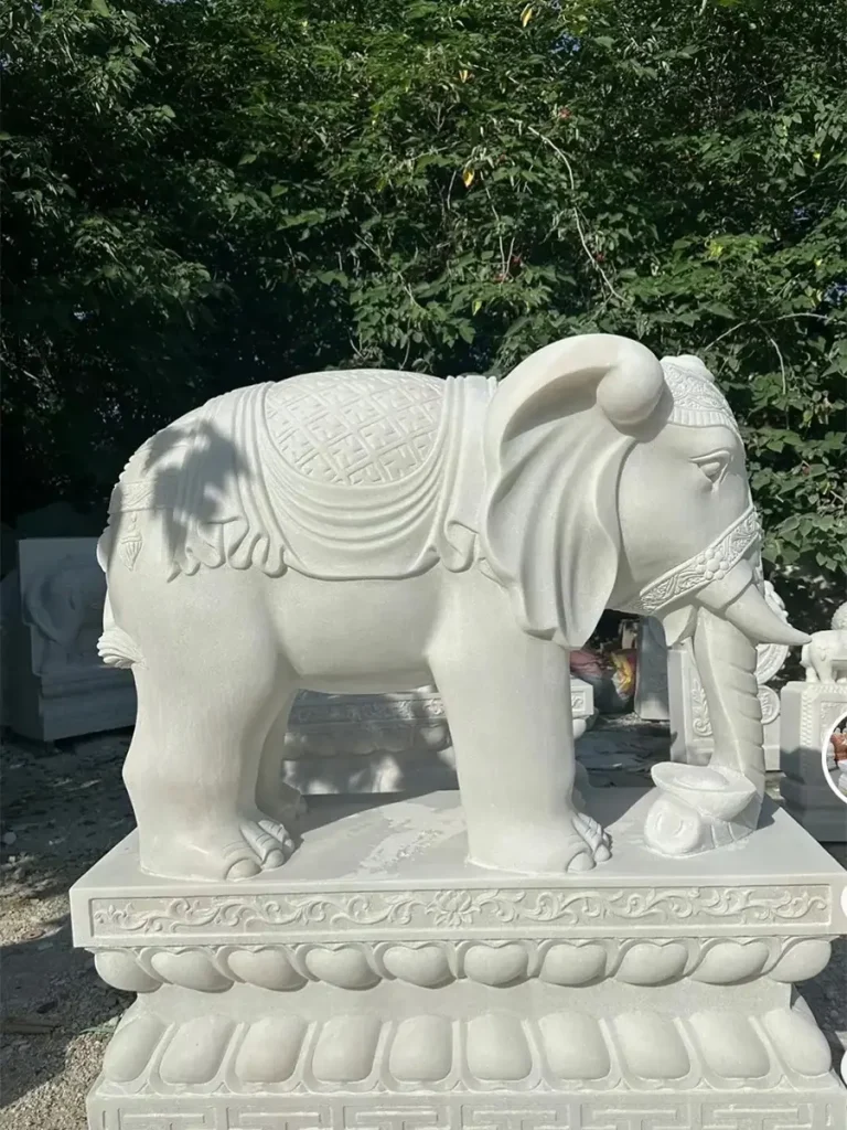 A magnificent life-size white marble elephant statue displayed in a stone workshop. Viewed from the side, the sculpture features intricate traditional blanket carvings, embodying the profound cross-cultural symbolism of wisdom, strength, and an extraordinary aura.