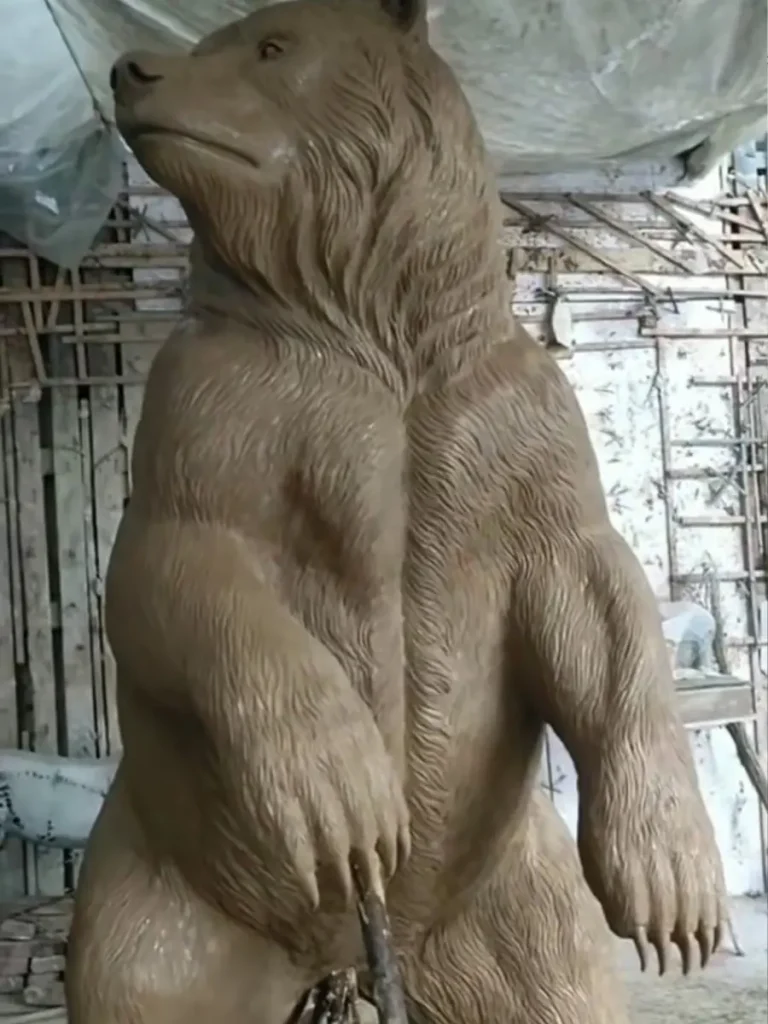 A detailed clay model of a life-size standing bear in a sculpture workshop. This crucial first step in the ancient lost-wax casting method allows artisans to sculpt the finest textures, capturing the raw muscle tension and the realistic grain of the fur before the bronze is poured.