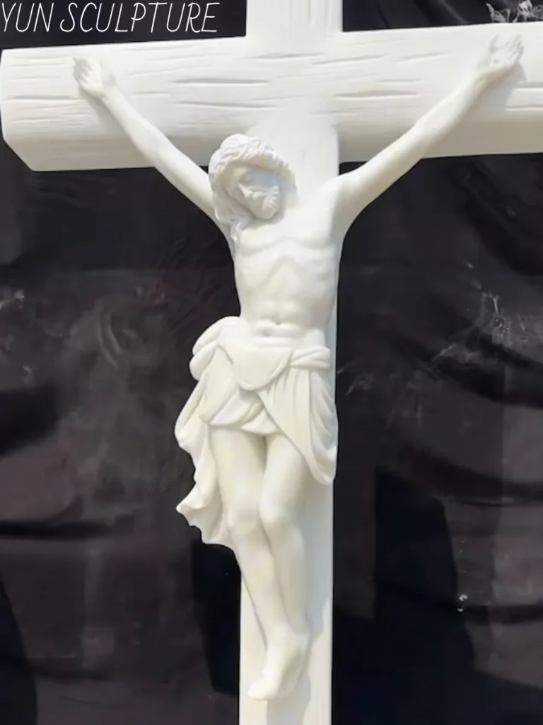 A close-up of a luminous white marble crucifix statue in a sculptor's workshop. Crafted from fine-grained stone like Carrara or Hanbaiyu, this exquisite piece holds the finest surface details, showcasing a cooler, more radiant aesthetic register that no bronze can replicate for indoor masterworks.