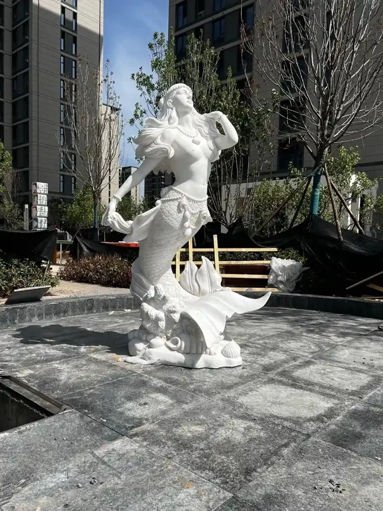 A high-angle shot of the white marble mermaid sculpture, highlighting how natural stone art elevates the aesthetic of a contemporary pool landscape.