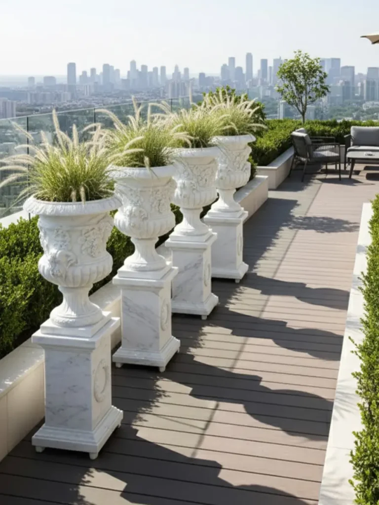 A row of large white marble garden urns on pedestals lining a rooftop terrace with a city skyline view, illustrating strategic placement for load-bearing and luxury aesthetic.