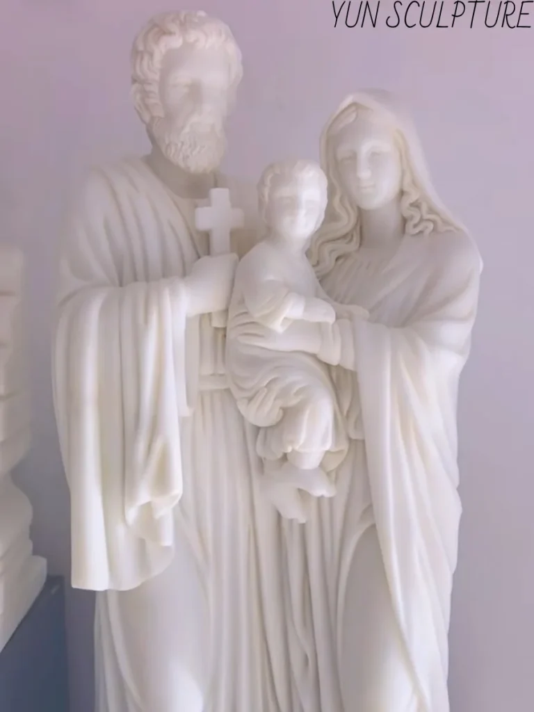 Close-up of a white marble Holy Family statue demonstrating the three-zone polishing system, with high luminous polish on the infant Jesus and matte finishes in the deep folds of the robes.