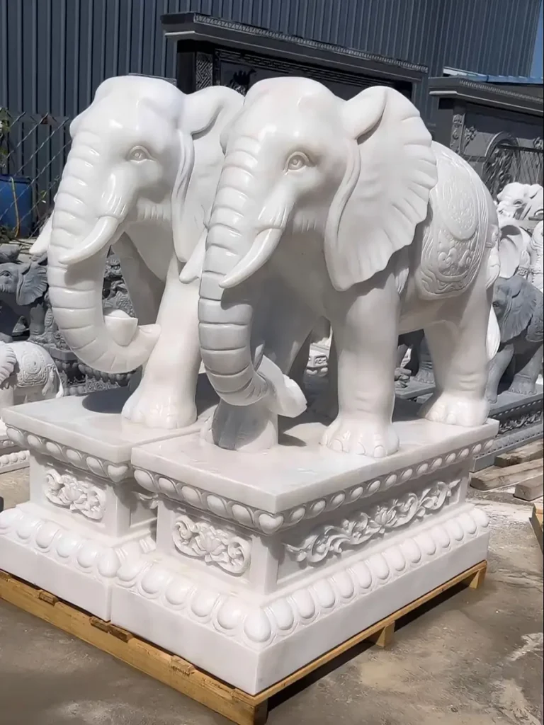A matching pair of premium life-size white marble elephant sculptures sitting on wooden pallets, ready for international shipping. In decorative arts, such grand and symmetrical installations symbolize profound memory, intelligence, and enduring stability.