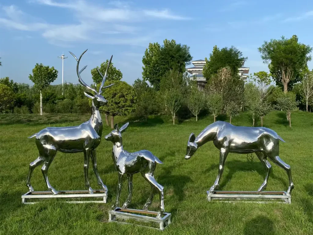 A heartwarming family of metal animal sculptures featuring a stag, doe, and fawn on a grassy field. The liquid silver reflections shift across their fluid surfaces throughout the day, ensuring these modern artworks become unforgettable emotional landmarks for visitors.