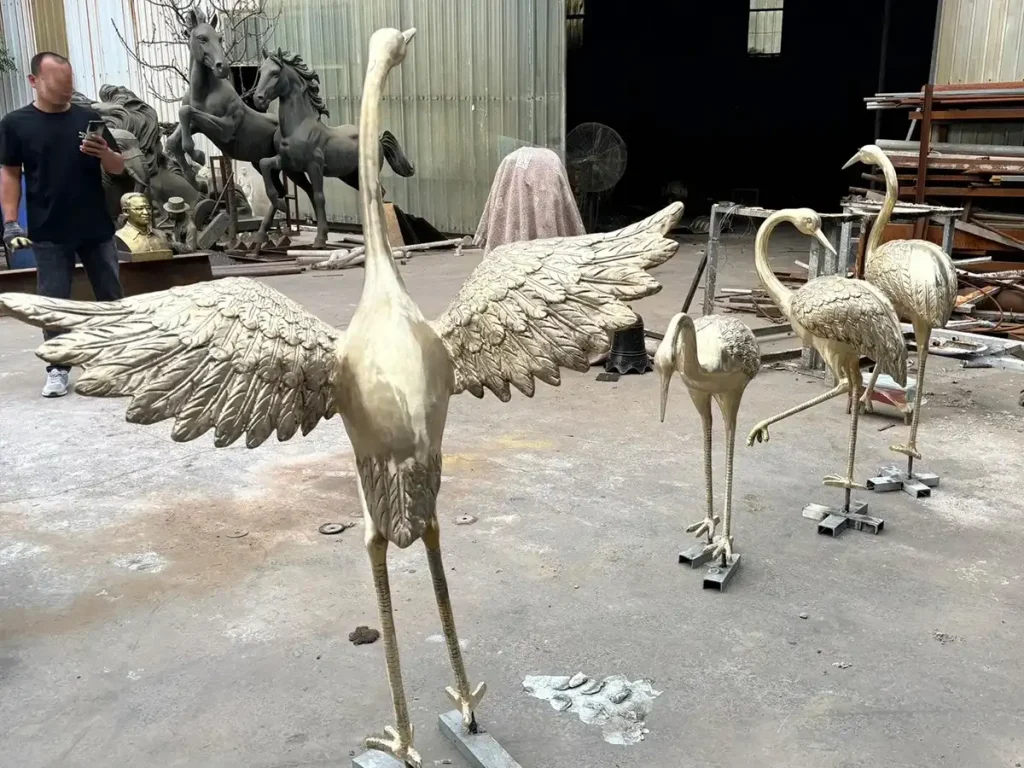 A dynamic metal crane statue with its wings fully extended, captured in a moment of elegant flight preparation. Placed alongside standing birds, this arrangement beautifully illustrates the harmony between stillness and motion essential to authentic Zen garden elements.