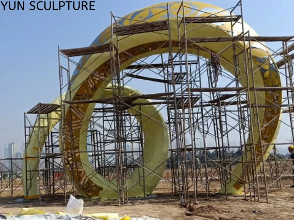 A large metal ring sculpture with scaffolding for final surface grinding and polishing, ensuring a seamless finish with no visible weld joints or heat-affected zones.