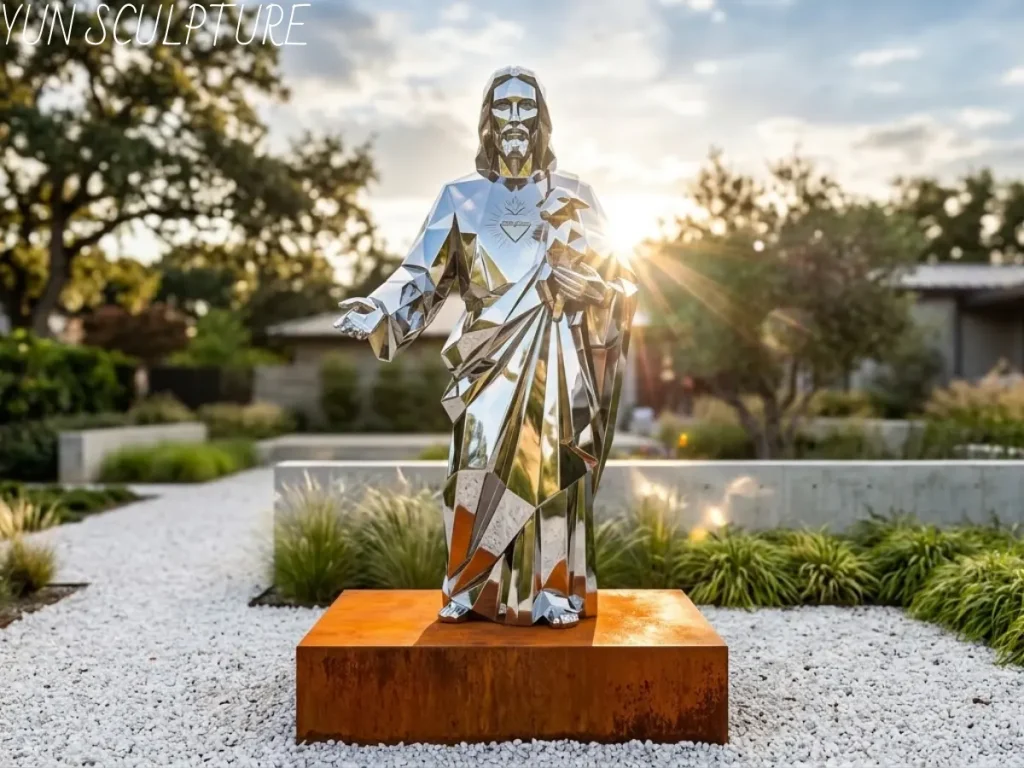 A full-body mirror-polished stainless steel Good Shepherd statue with outstretched arms, standing in a contemporary gravel garden with a rising sun background.