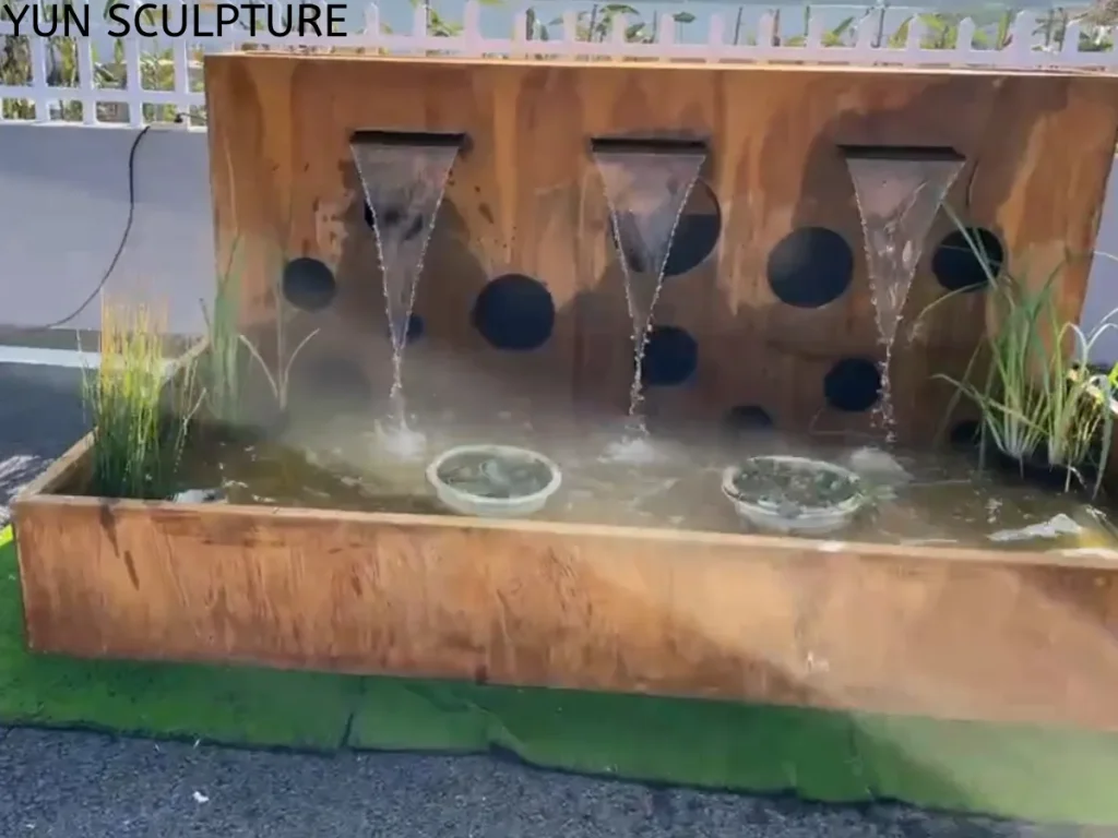 Frontal view of a flowing Corten steel water feature functioning as a dynamic planter-pond. With water splashing gently among the potted aquatic grasses, the setup illustrates a layered narrative where plants act as functional components for natural filtration and oxygenation, ultimately enhancing the ecological value of the garden.