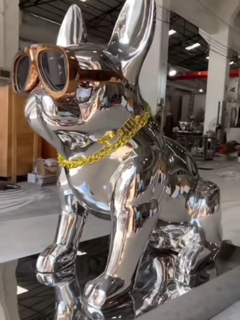 Side view of a modern metal French Bulldog sculpture with a high-gloss mirror finish, showcasing custom accessories.