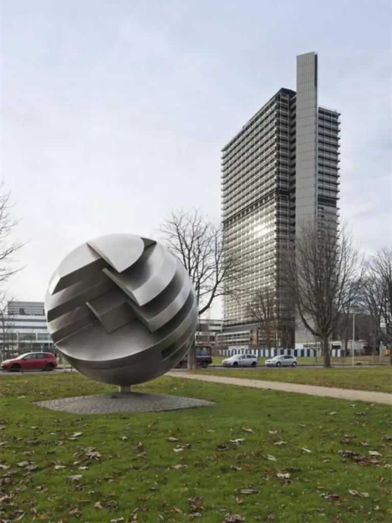 A mid-range view of a custom-fabricated geometric metal sculpture featuring deep, layered cutouts. Set against the rigid structural grid of a modern corporate building, the spherical artwork brilliantly combines structural logic with artistic expression, proving how well-designed installations become an integral part of the architecture itself.
