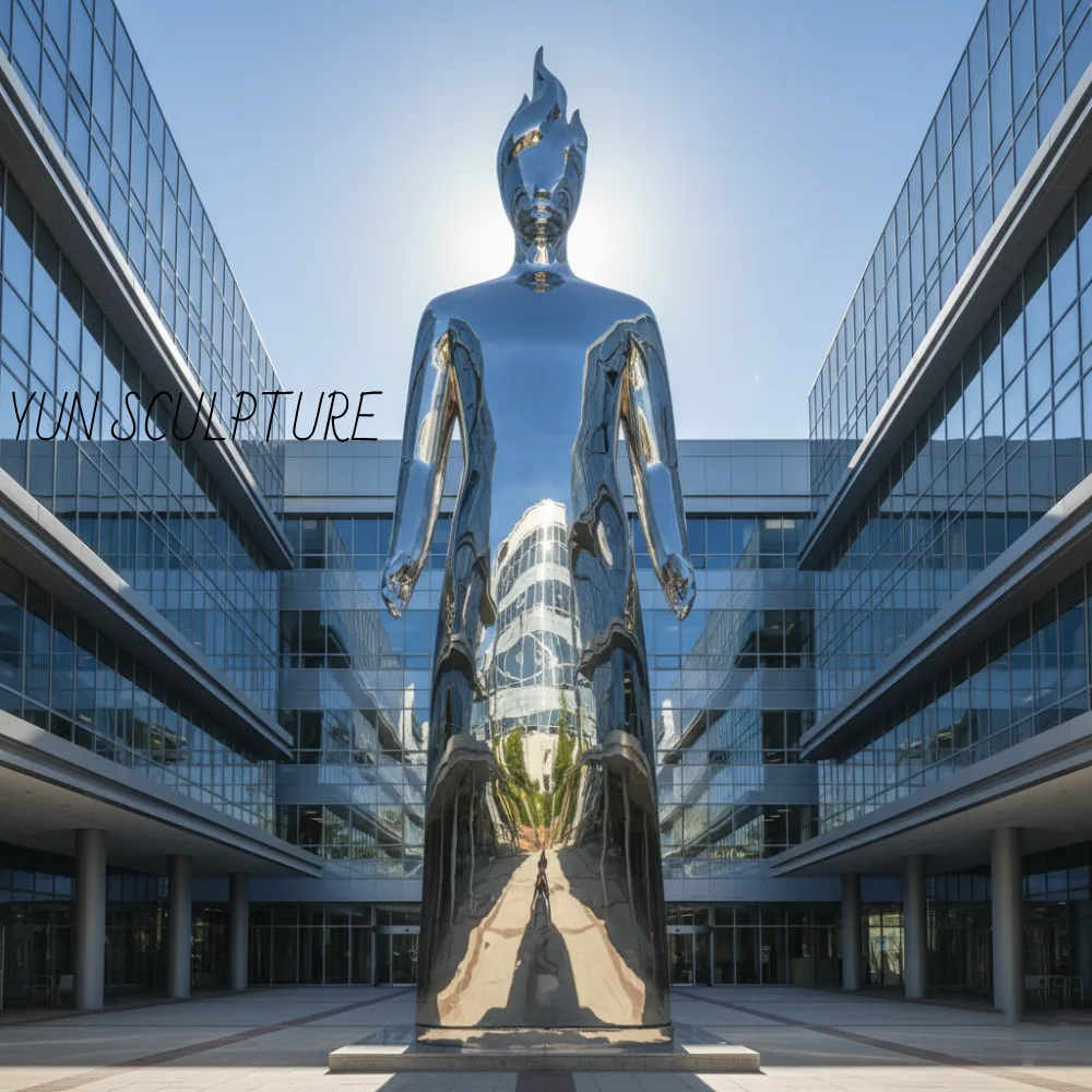 A monumental 316-grade stainless steel St. Jude statue with a mirror polish finish, showcasing the structurally independent flame element in a modern medical facility courtyard.