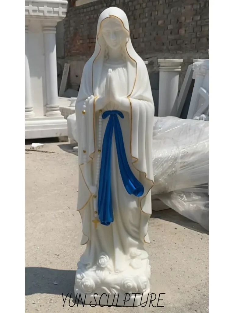 A full-length, majestic white marble our lady of lourdes statue france replica standing proudly outdoors. Crafted with rigorous classical training and exquisite drapery, this monumental stone sculpture represents the massive 19th-century wave of artistic replication fueled by skilled Italian marble exports, designed to recreate the exact spiritual dynamics of the Massabielle shrine for parishes worldwide.