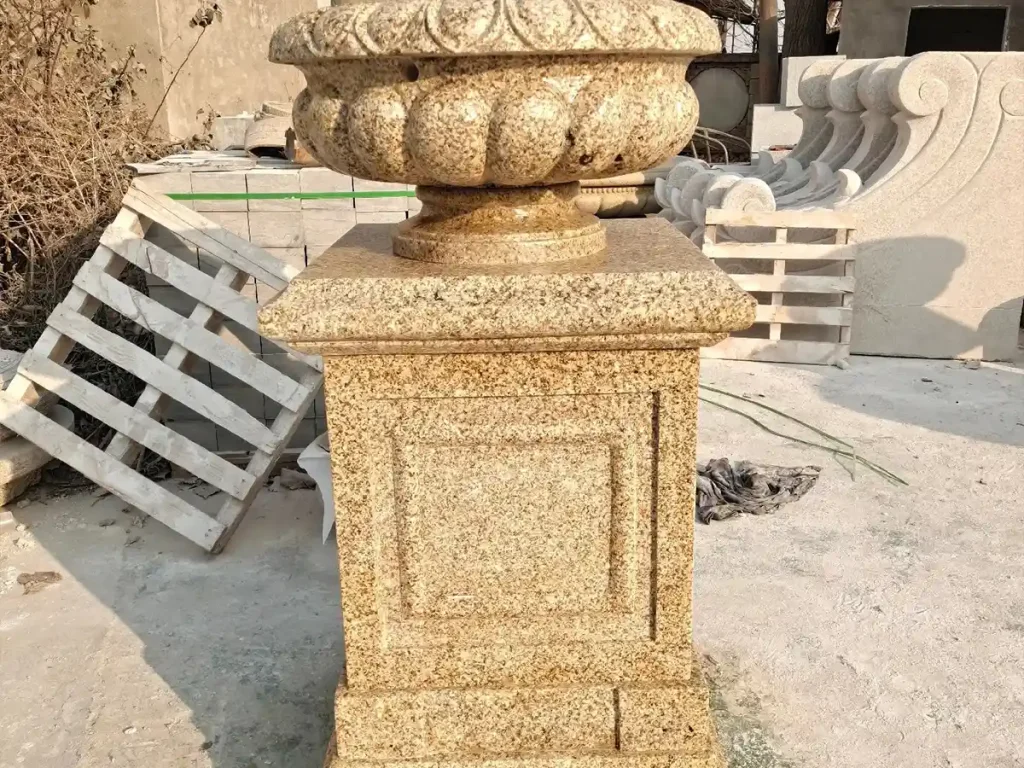 A classic natural stone garden urn on a pedestal made of durable yellow granite, perfect for establishing permanent visual authority in historic estate gardens.