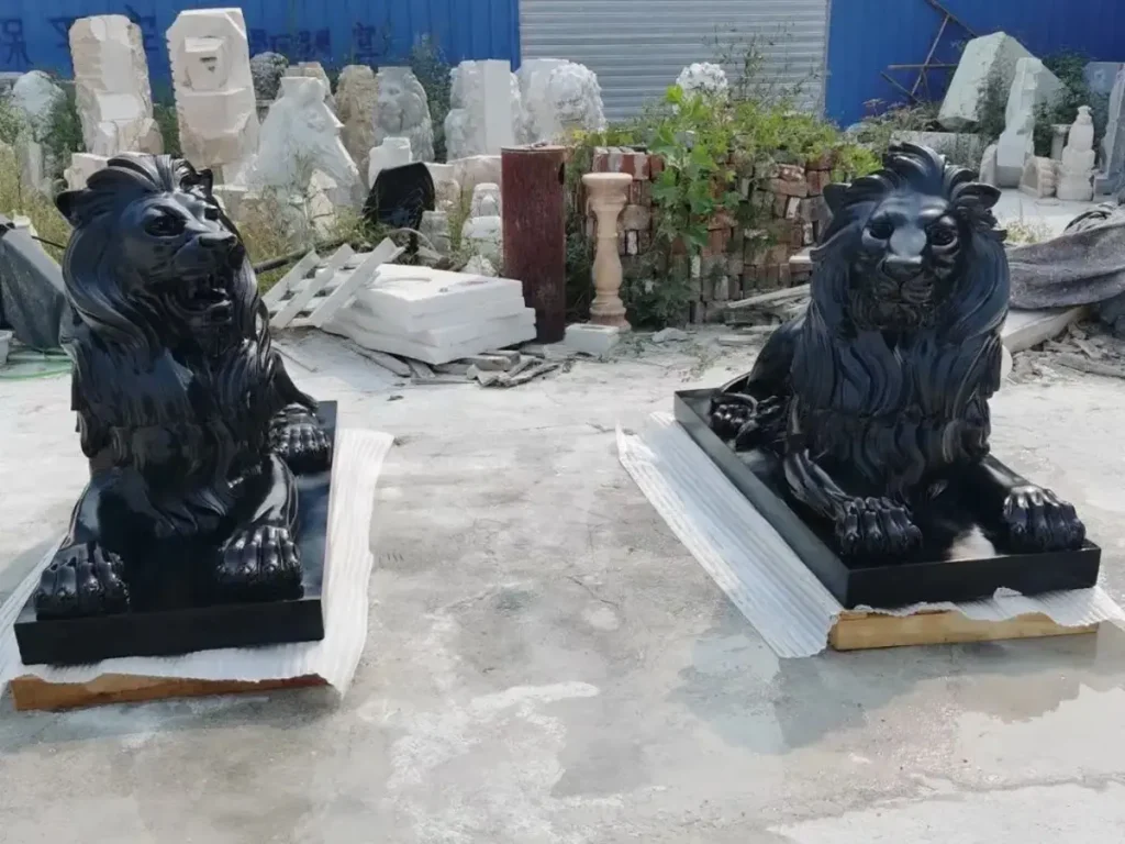 A symmetrical pair of large black stone guardian lion statues in a resting posture, showcasing classical realism and muscular definition.