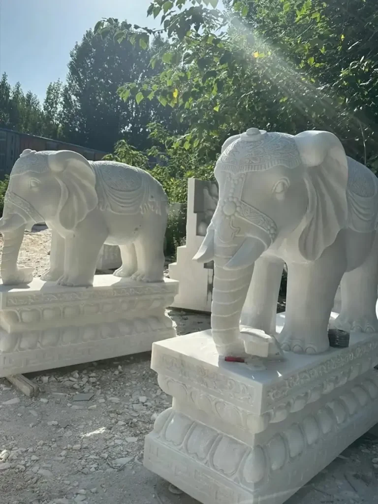 Two newly crafted, life-size white marble elephant statues standing in a factory yard. These monumental sculptures showcase the remarkable scale and physical mass that give elephants their rich symbolic meaning in architectural and decorative arts.