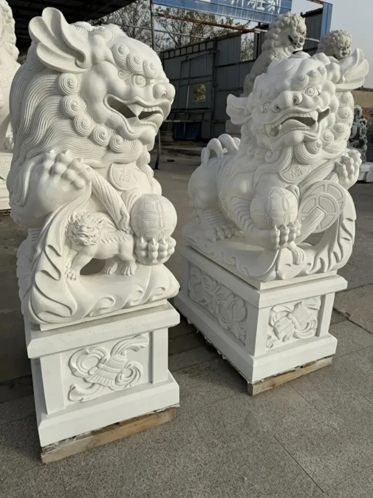 A vibrant pair of white premium granite Foo Dogs in a Hui'an workshop. These lively Southern style sculptures feature agile postures, wide open mouths, and highly detailed facial expressions, resting on ornate rectangular stone bases.